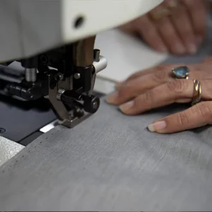 Dettaglio di una macchina da cucire industriale durante la lavorazione di un tessuto grigio
