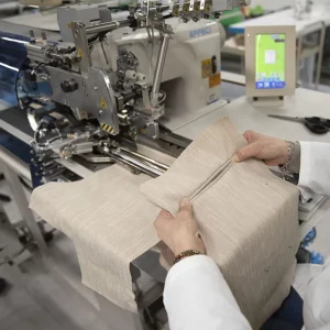 Operatore al lavoro su tessuto chiaro con macchinari industriali per la confezione