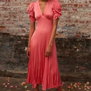 Modella con abito lungo rosa corallo davanti a una parete in mattoni