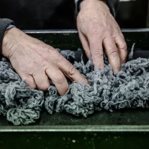 Mani di un operatore durante la lavorazione manuale di materiale tessile su un piano di lavoro