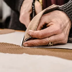 Mani di un sarto durante la cucitura manuale di un tessuto su un piano di lavoro
